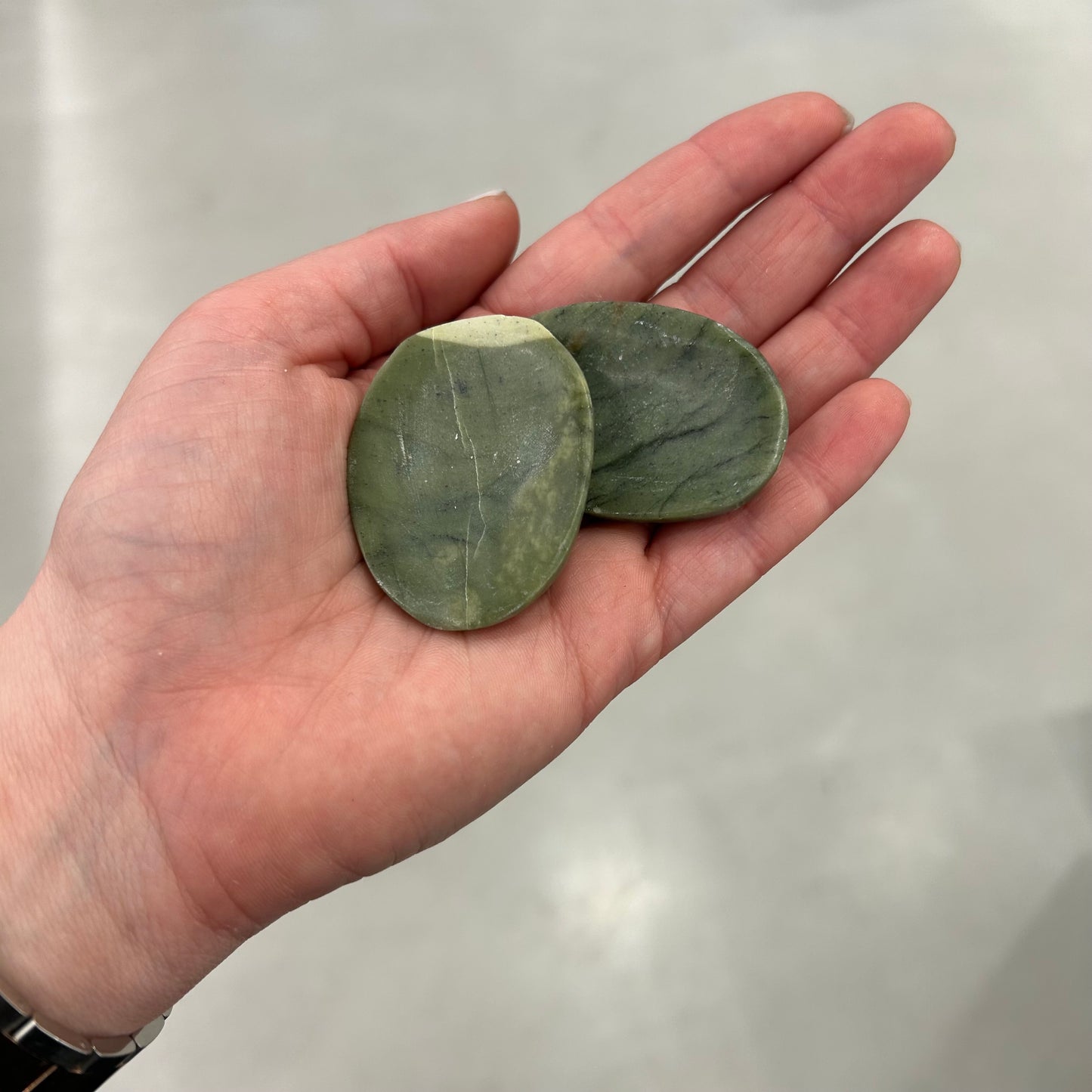 Hand holding two jade worry stones symbolizing tranquility, protection, and good luck.