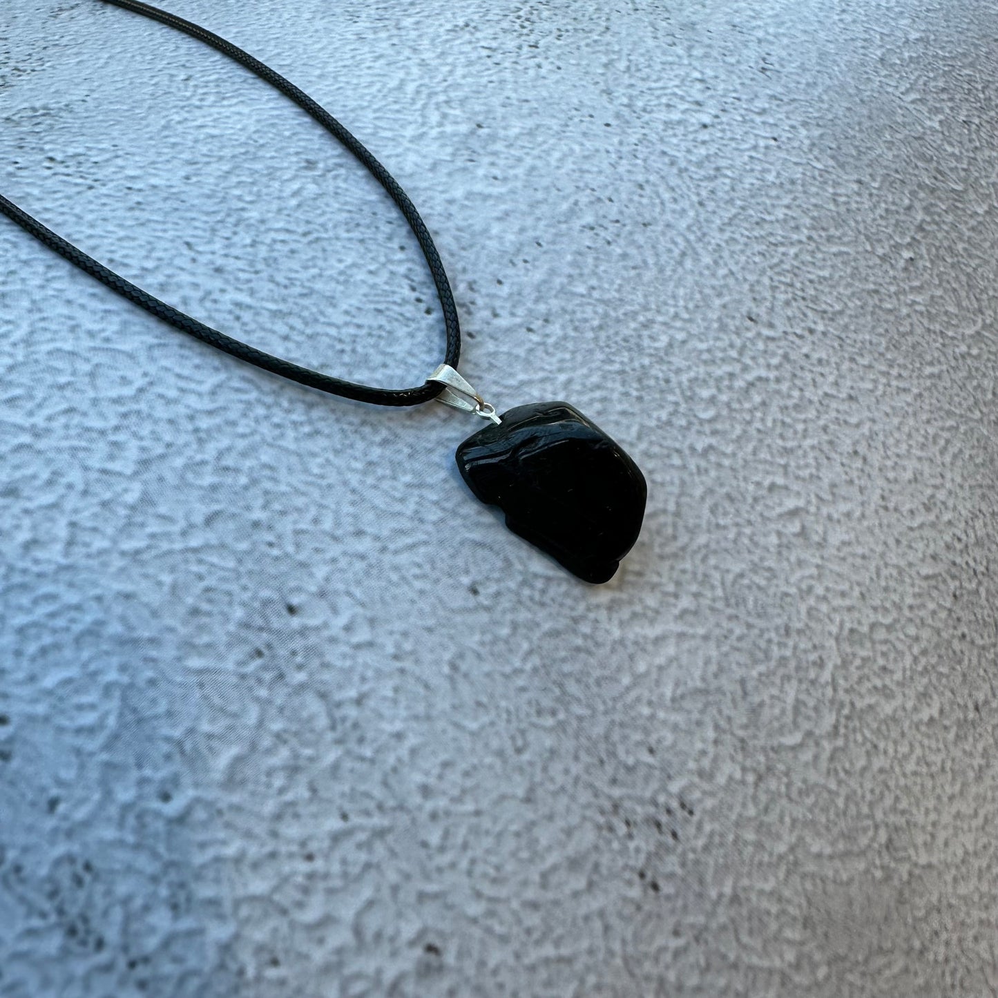 Black Tourmaline tumbled stone pendant necklace on textured surface, protective and grounding jewelry piece.