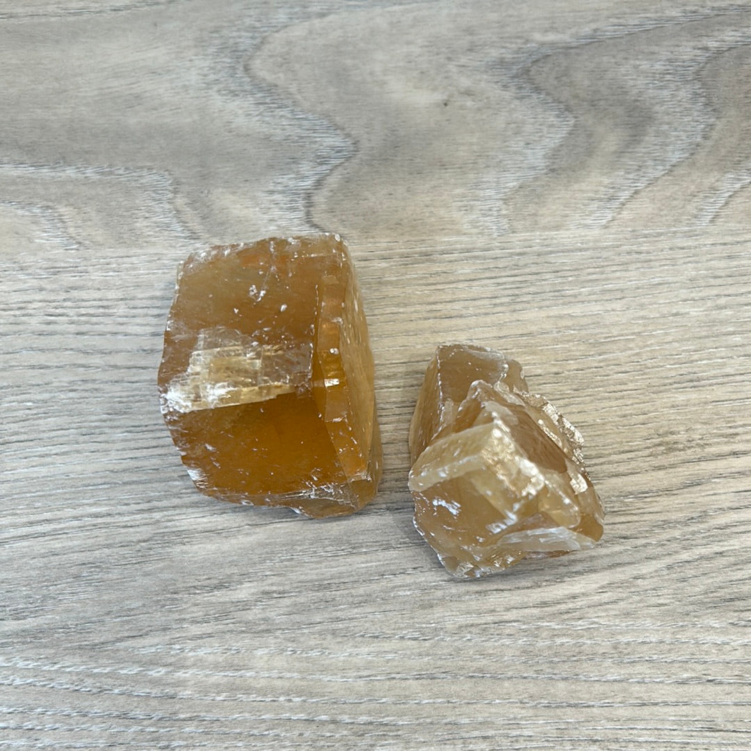 Two rough pieces of Honey Calcite showcasing their golden hue and natural texture, promoting confidence and positive energy.