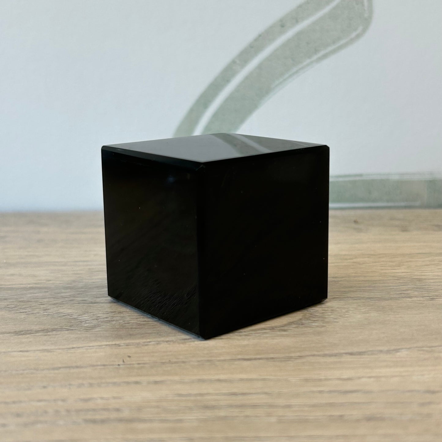 Black obsidian cube, 1.7 inches, known for protection and stress relief, placed on a wooden surface.
