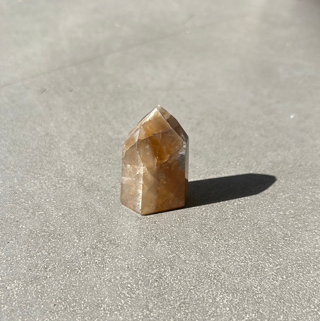 Citrine tower crystal on a gray surface, known for attracting wealth and enhancing intuition.