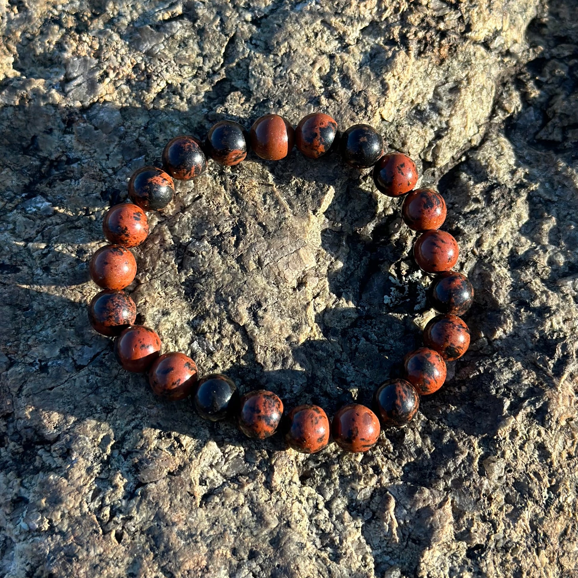 Mahogany Obsidian bracelet 8MM on textured rock surface, showcasing natural healing properties and polished finish.