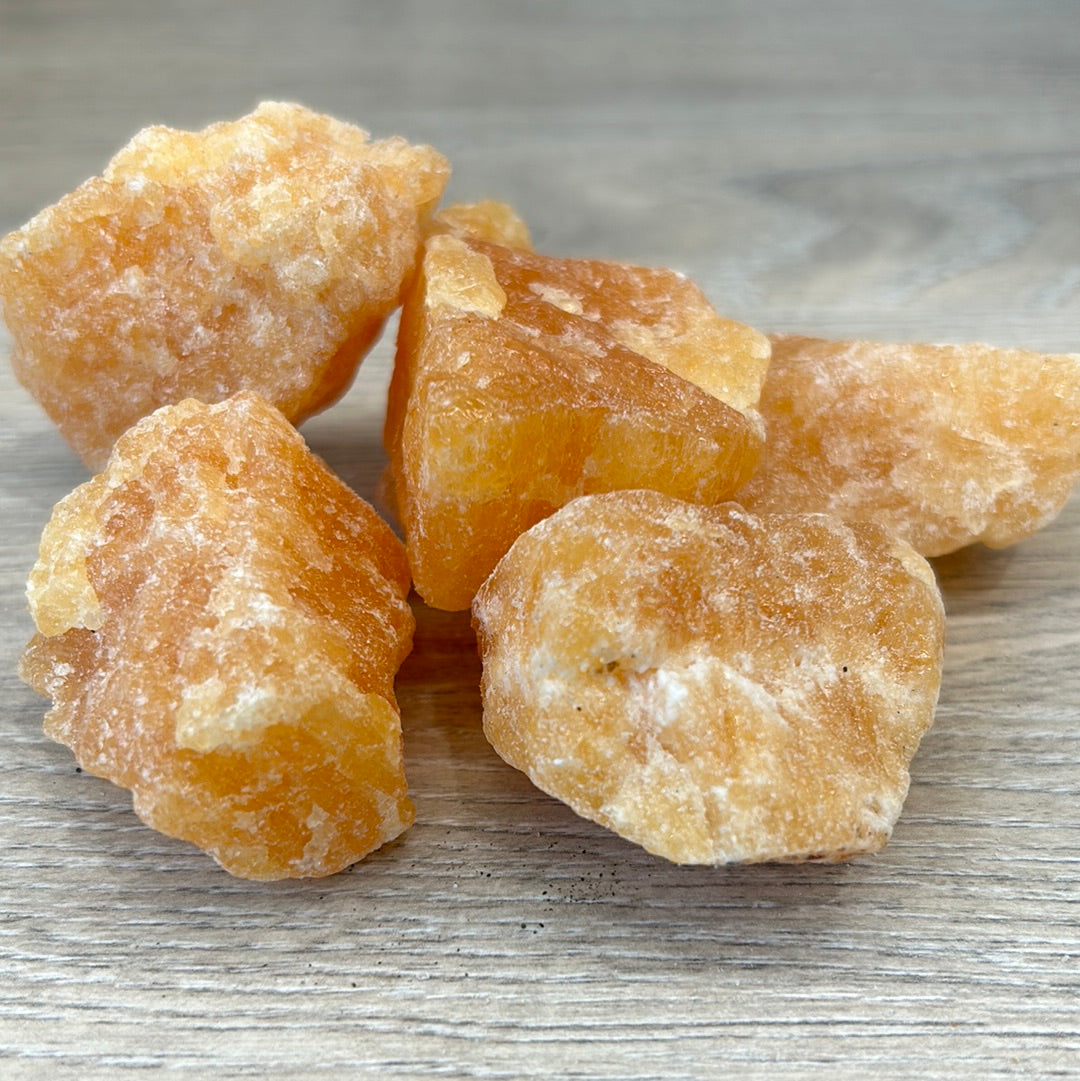 Rough orange calcite crystals grouped on a wooden surface, promoting healing and calming energy in any space.