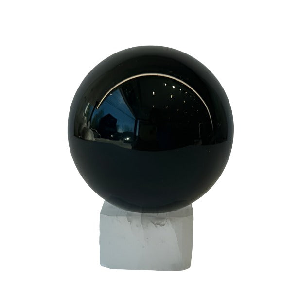 Medium Rainbow Obsidian Sphere displayed on a sleek white stand, showcasing its glossy black surface and unique iridescence.