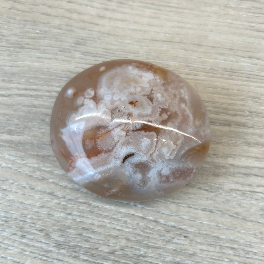 Flower Agate Palm Stone with light pink hues and delicate inclusions on wooden surface.