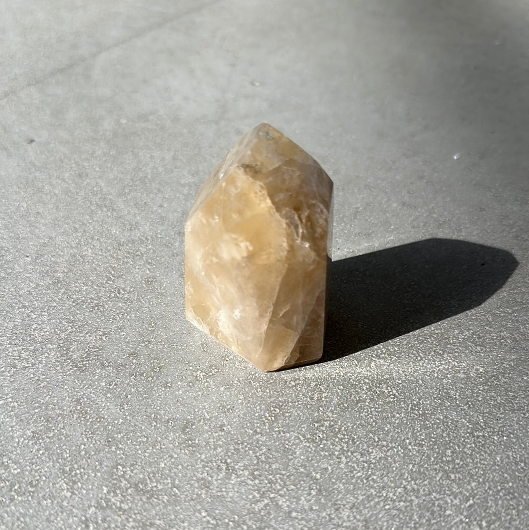 Citrine tower crystal on a textured surface, known for attracting wealth and boosting self-confidence.