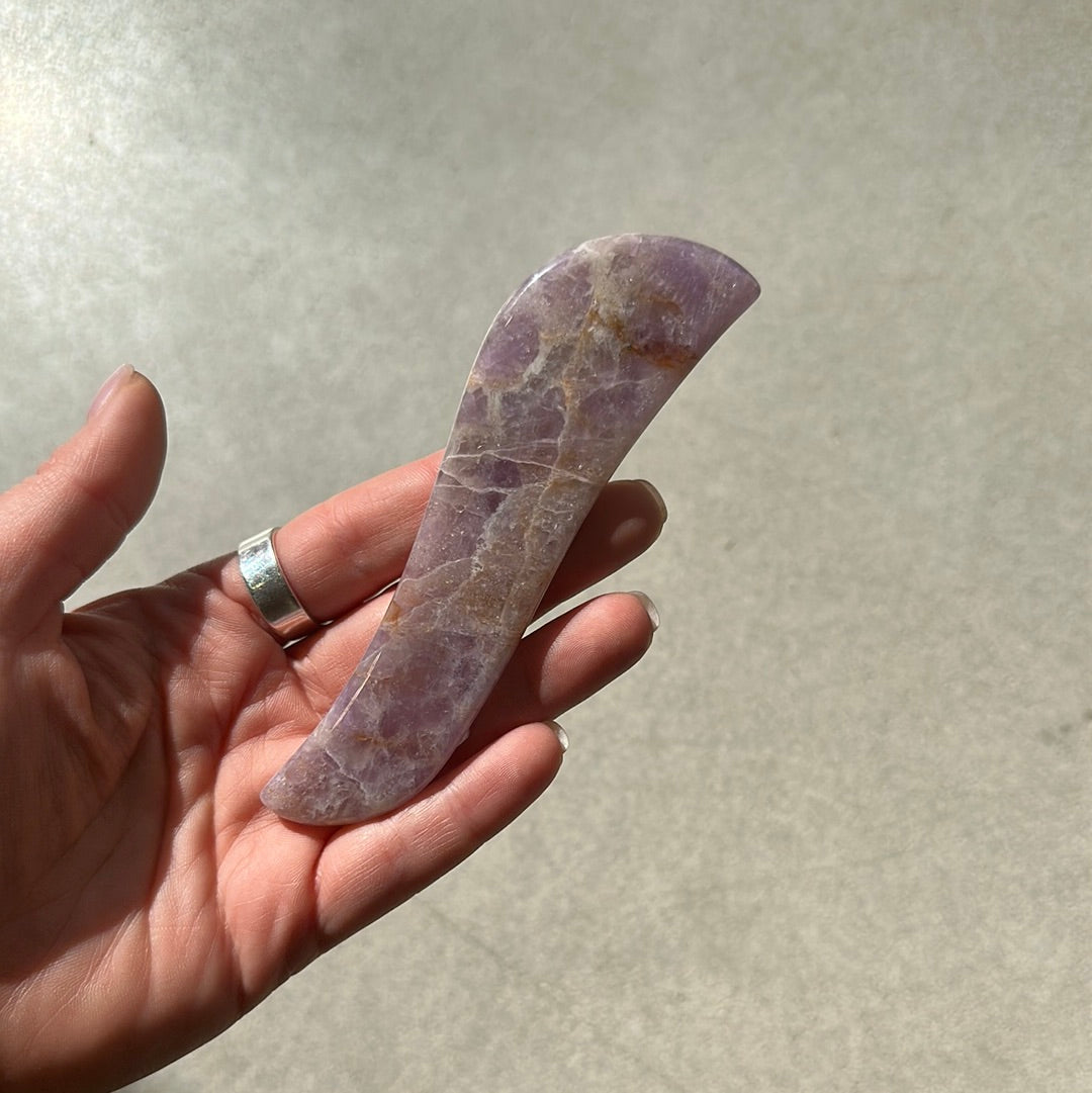 Chevron Amethyst Gua Sha healing crystal held in a hand, used for stress relief and mood stabilization.