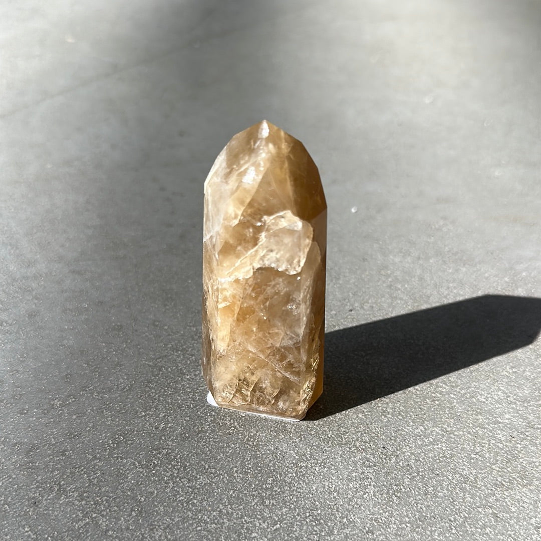 Citrine tower crystal on a dark surface, known for attracting wealth and enhancing intuition.
