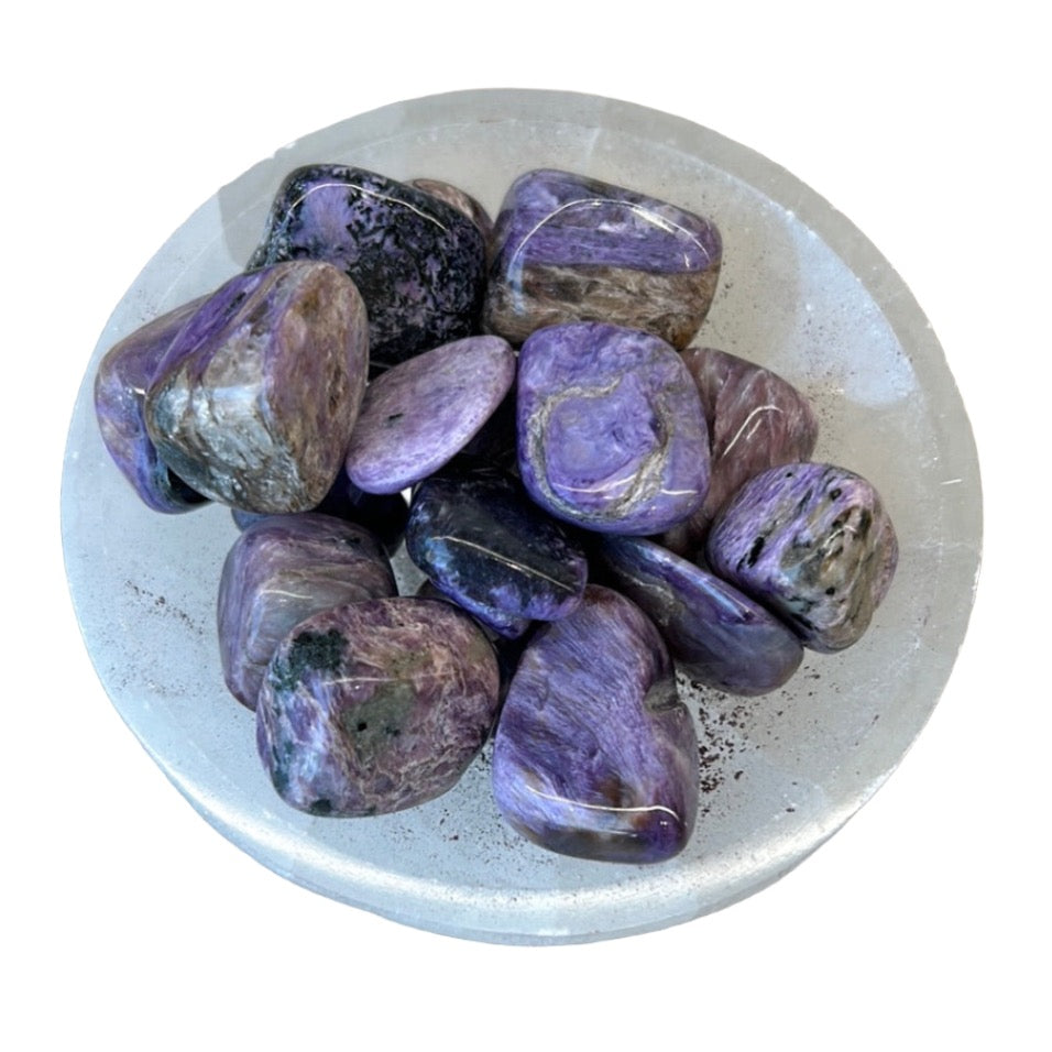 Charoite tumbled stones on a white dish, believed to transform energy and reduce stress.