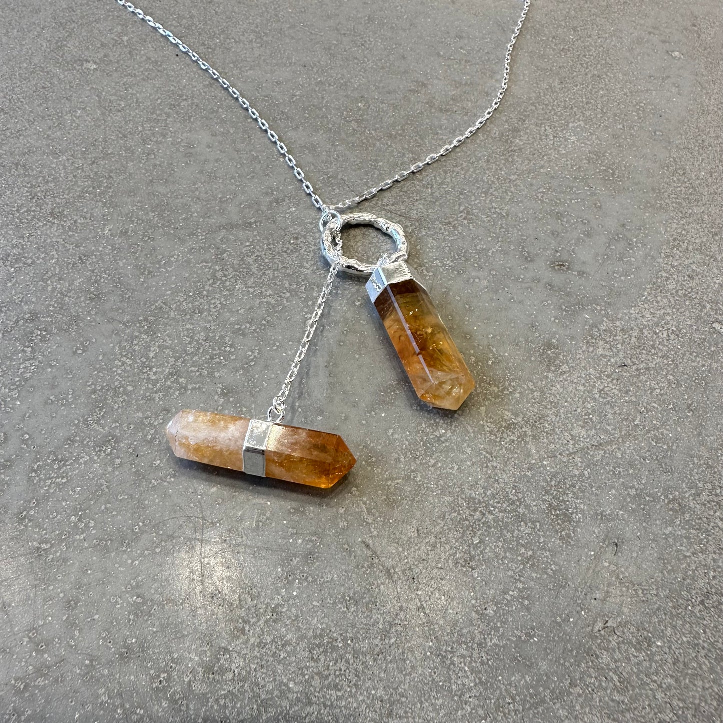Citrine double point necklace on a gray surface, showcasing energizing crystal and silver chain design.