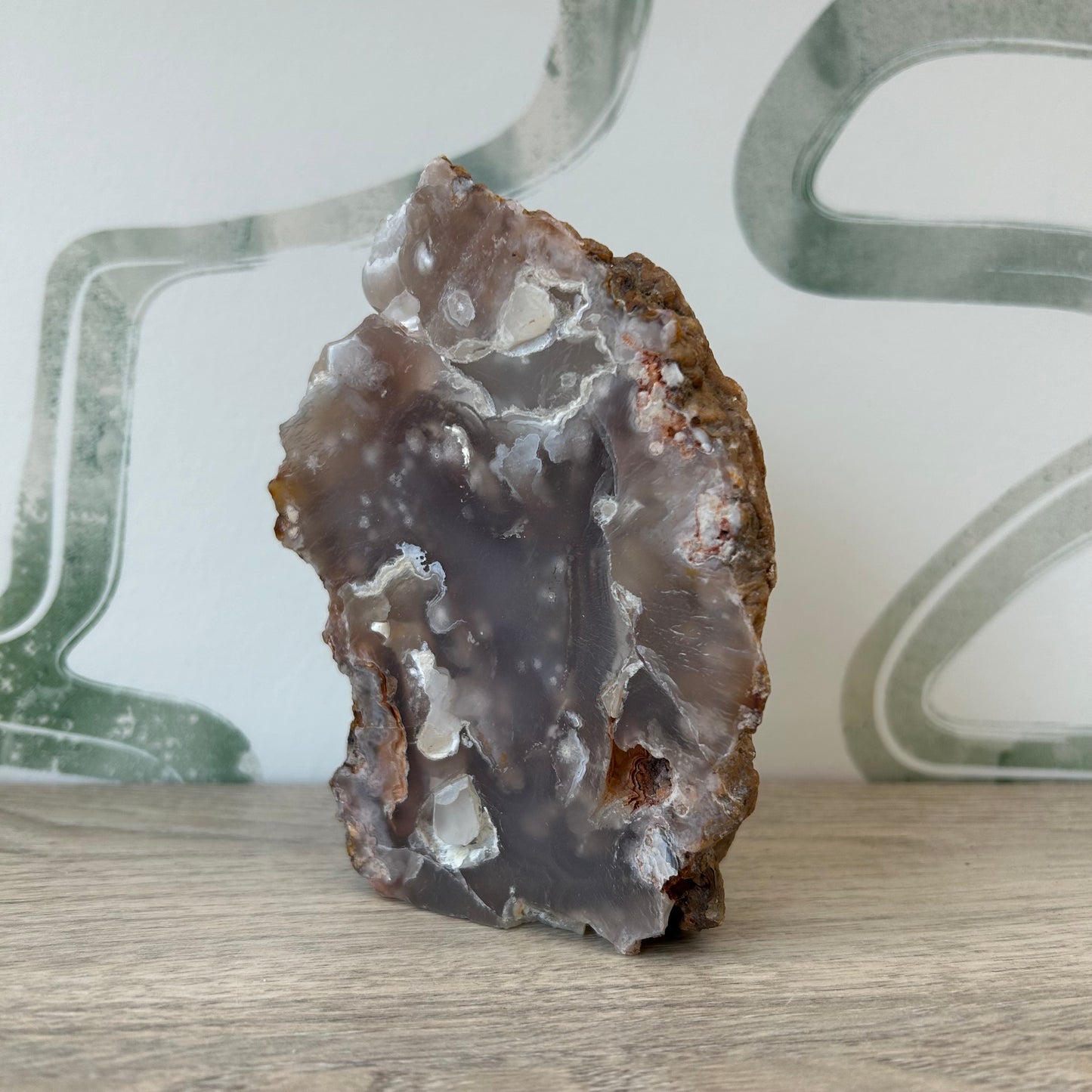 Raw agate crystal with natural earthy tones and unique patterns on a wooden surface, set against an abstract green and white background.