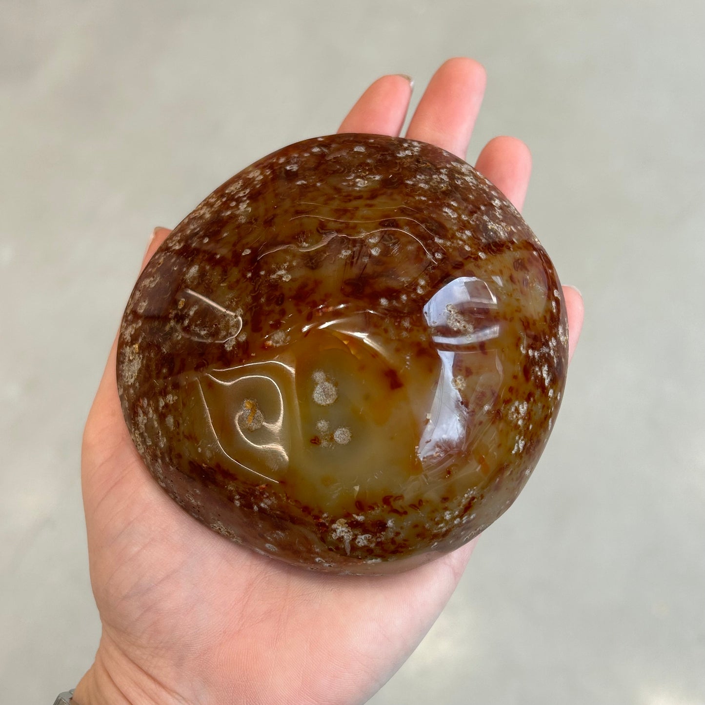 Hand holding polished agate geode, showcasing its glossy surface and natural patterns, known for balancing and cleansing properties.