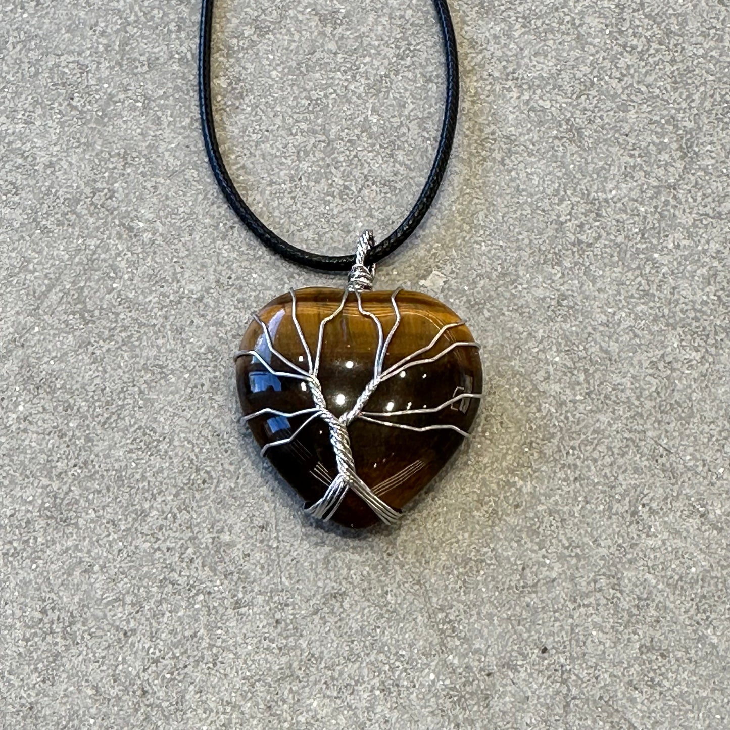 Tiger Eye pendant necklace featuring a heart-shaped stone with a silver tree design on a black cord.