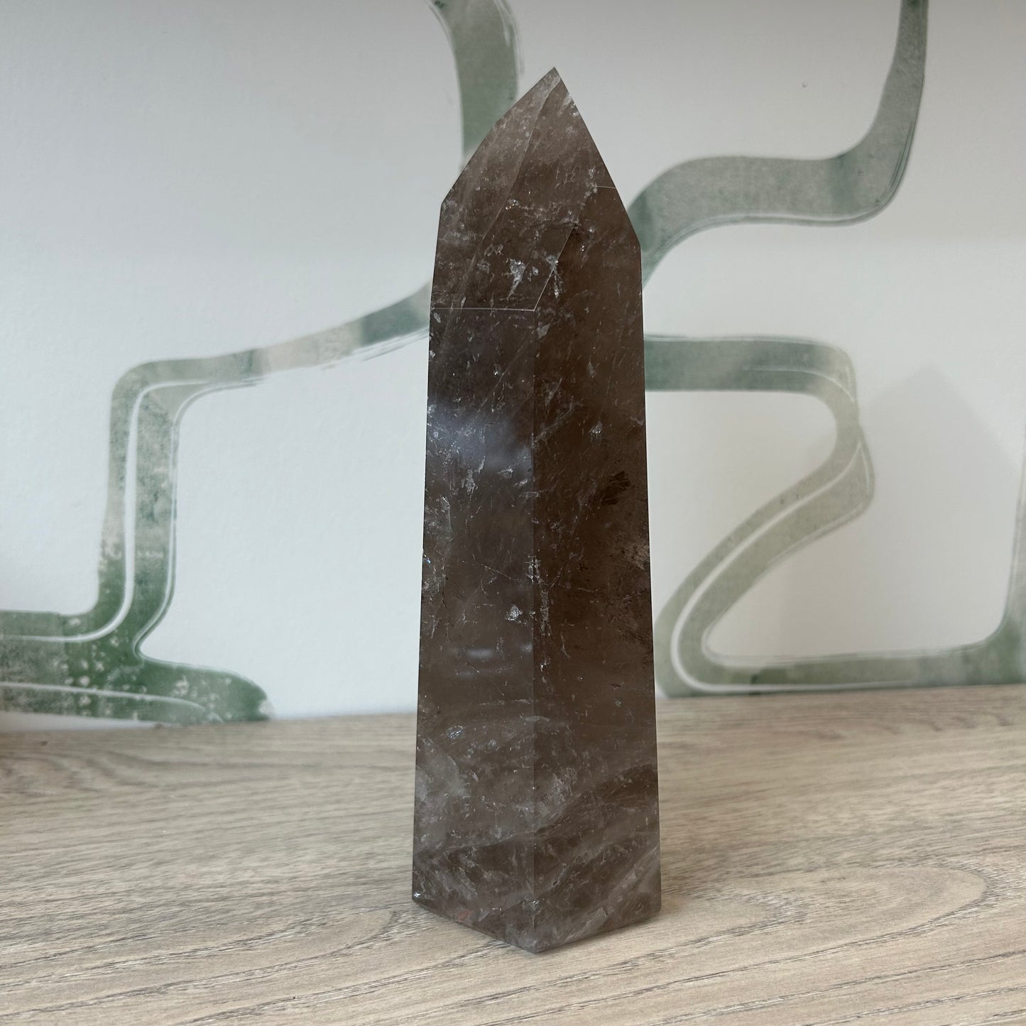 Smoky Quartz tower crystal standing on a wooden surface, known for grounding and purifying negative energies.