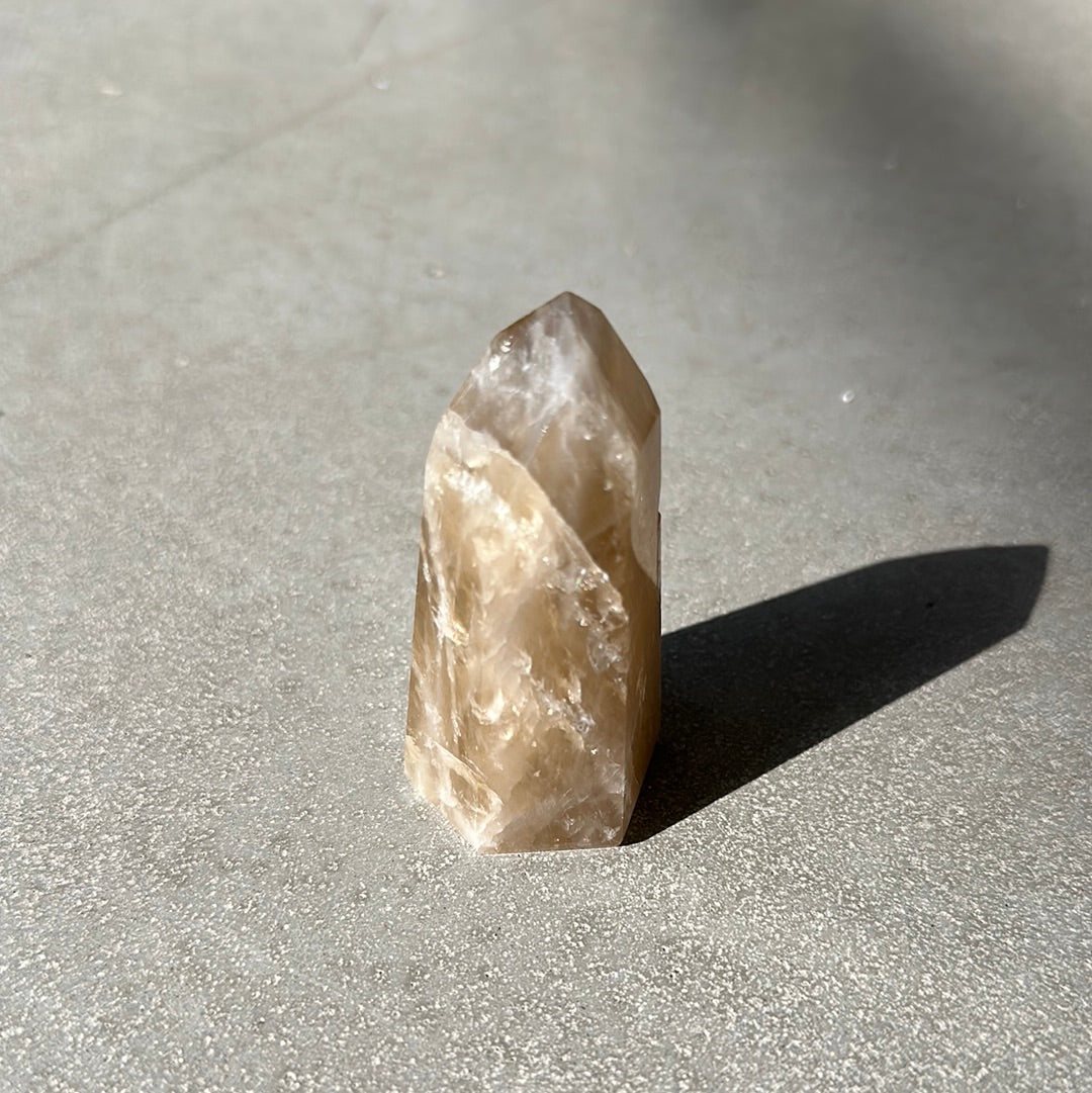 Citrine tower crystal on a gray surface, known for enhancing intuition and attracting prosperity.