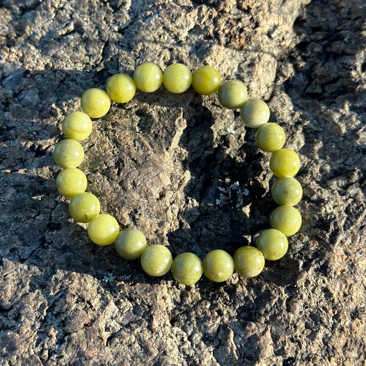 8MM jade bracelet showcasing genuine jade beads on a textured rock surface, emphasizing its beauty and healing properties.