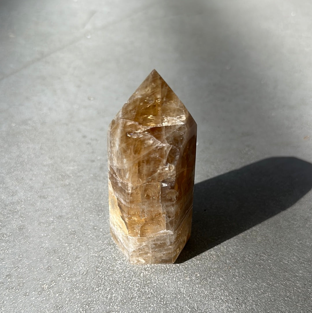 Citrine tower crystal known for energizing life and enhancing intuition, on a textured surface.