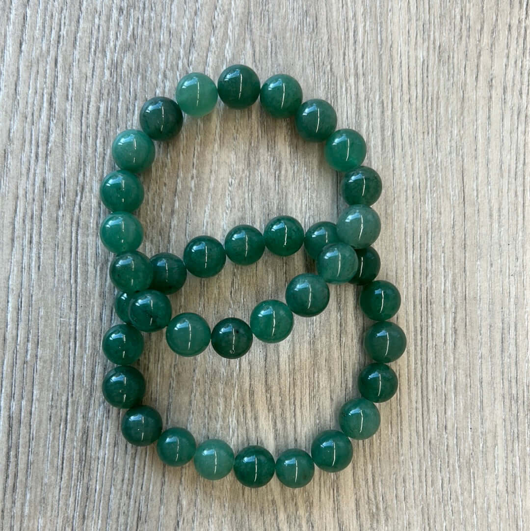 Green Aventurine bracelet with 10mm beads for balance and harmony, placed on a wooden surface.