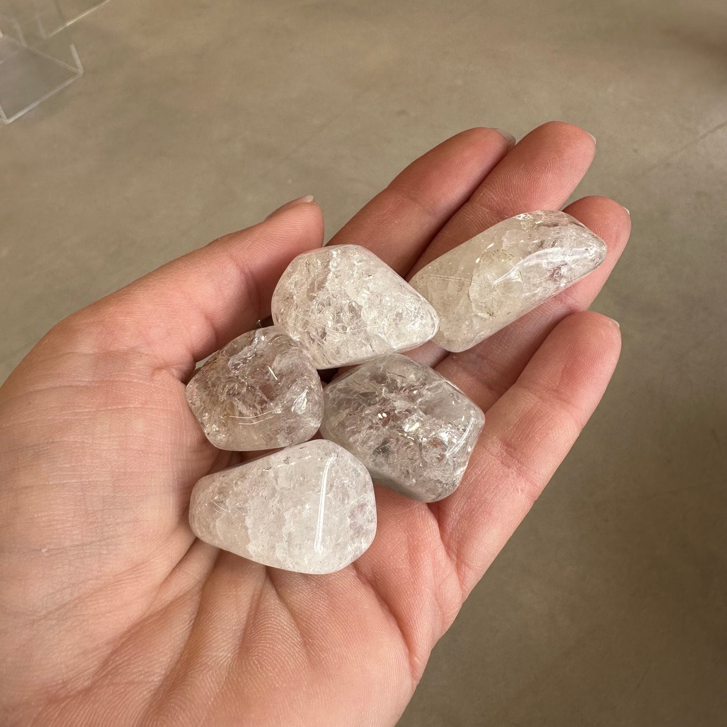 Hand holding five cracked clear quartz tumbled stones, known for energy amplification and balance.
