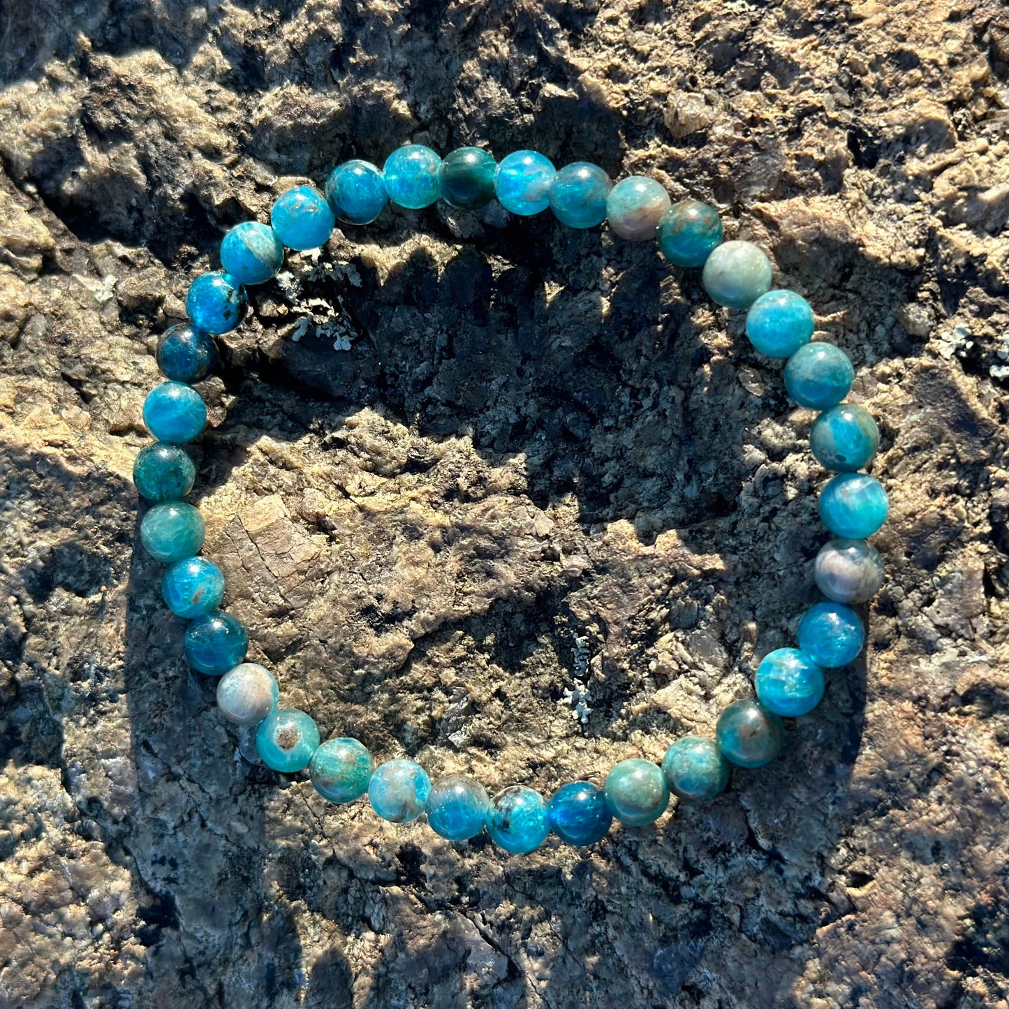 Blue Apatite bracelet with natural semi-precious stones on textured rock, promotes chakra balance, creativity, and communication.