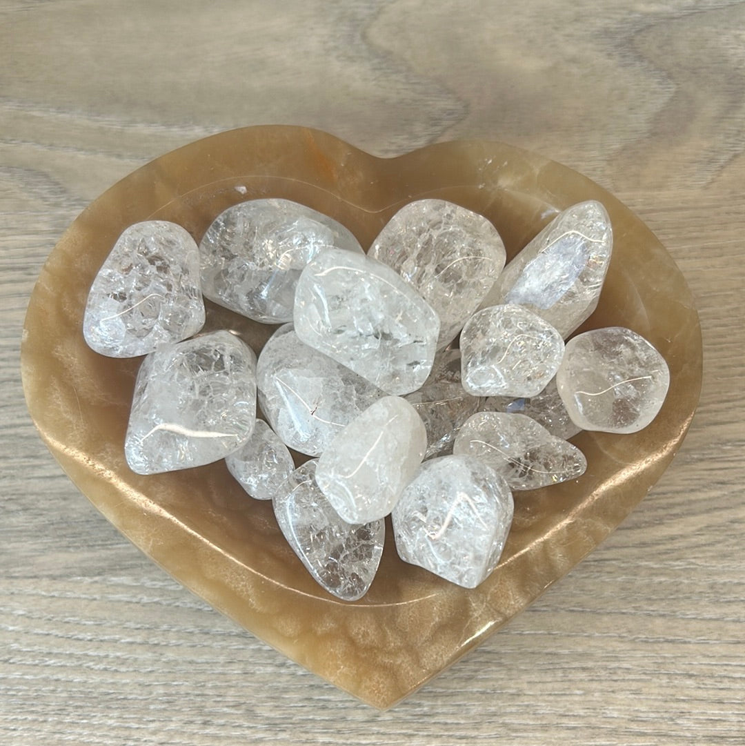 Heart-shaped bowl with cracked clear quartz tumbled stones on wooden surface.