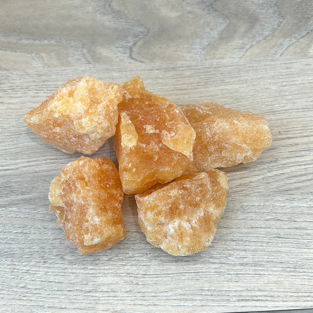 Five pieces of rough orange calcite, showcasing healing properties and natural textures on a wooden surface.