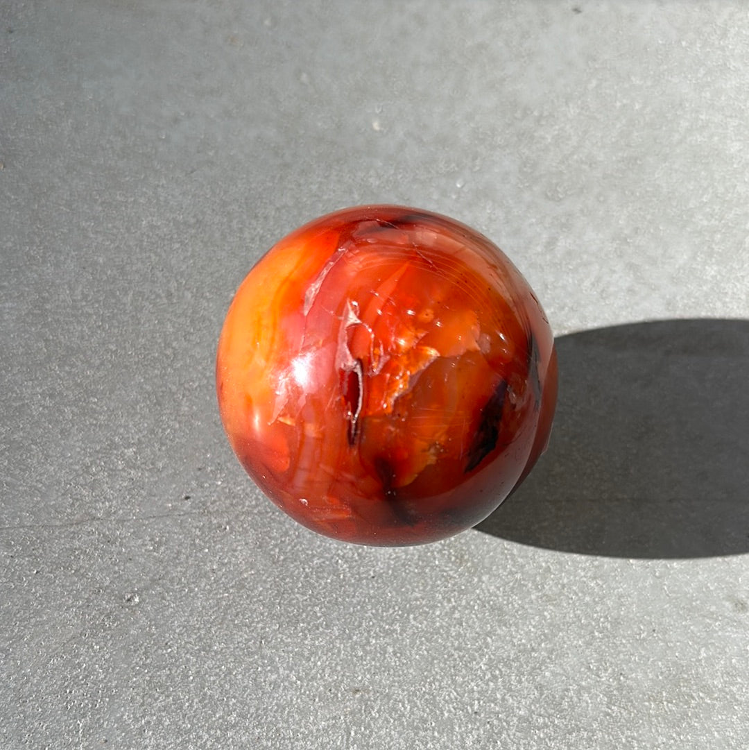 Polished carnelian sphere weighing 487g, promoting creativity, vitality, and healing properties in a natural setting.