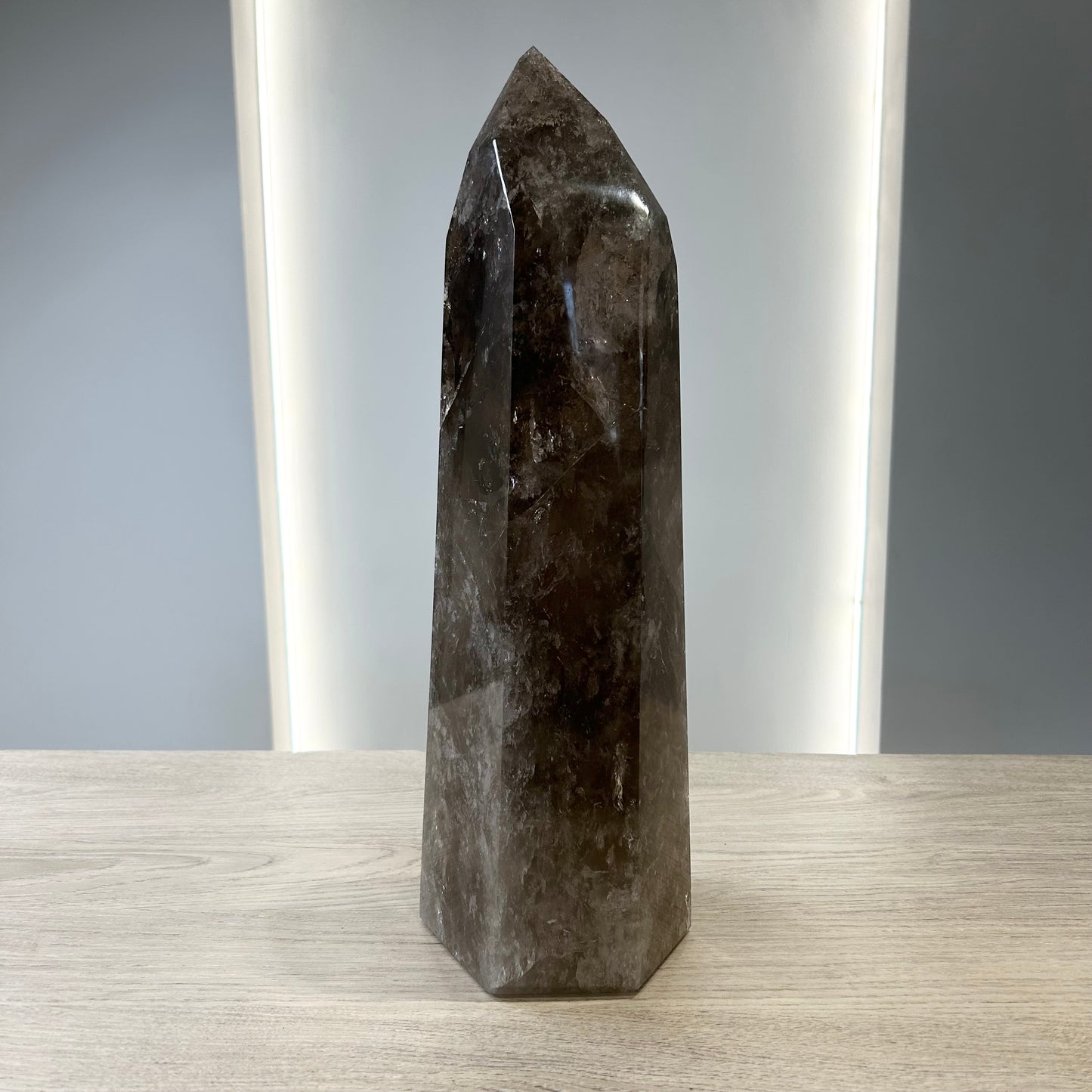 Smoky Quartz Tower crystal displaying grounding properties and neutralizing negative energies on a wooden surface.