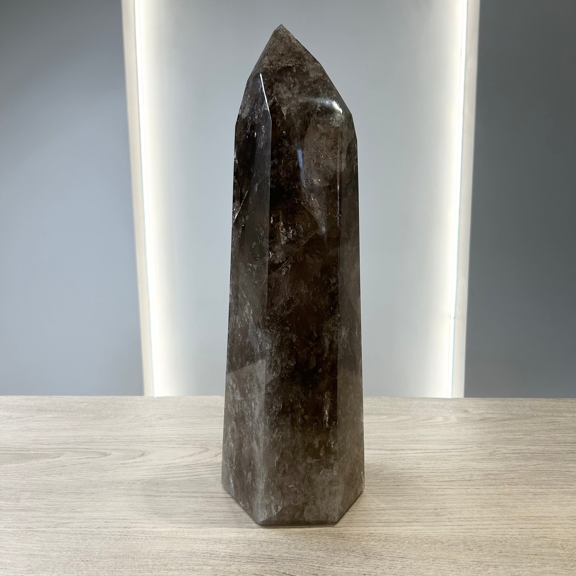 Smoky Quartz Tower crystal displaying grounding properties and neutralizing negative energies on a wooden surface.