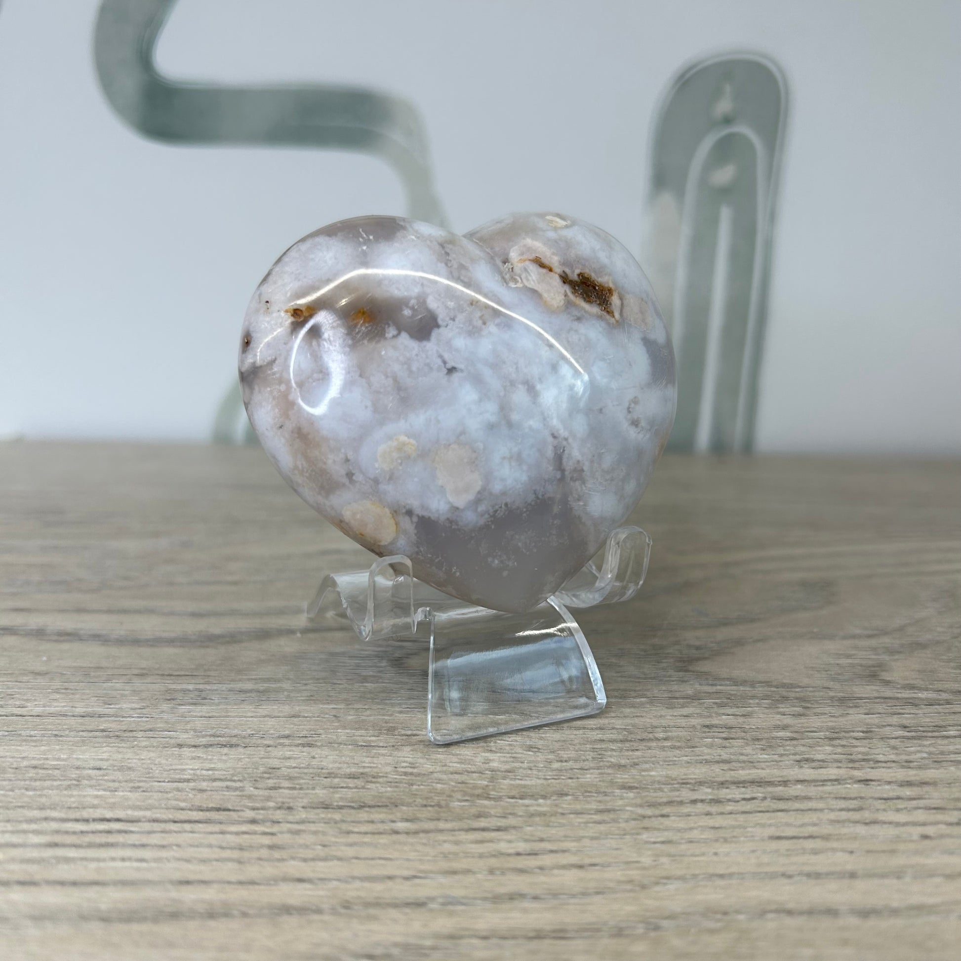 Heart-shaped Flower Agate crystal with light pink hues and delicate inclusions on a clear stand.