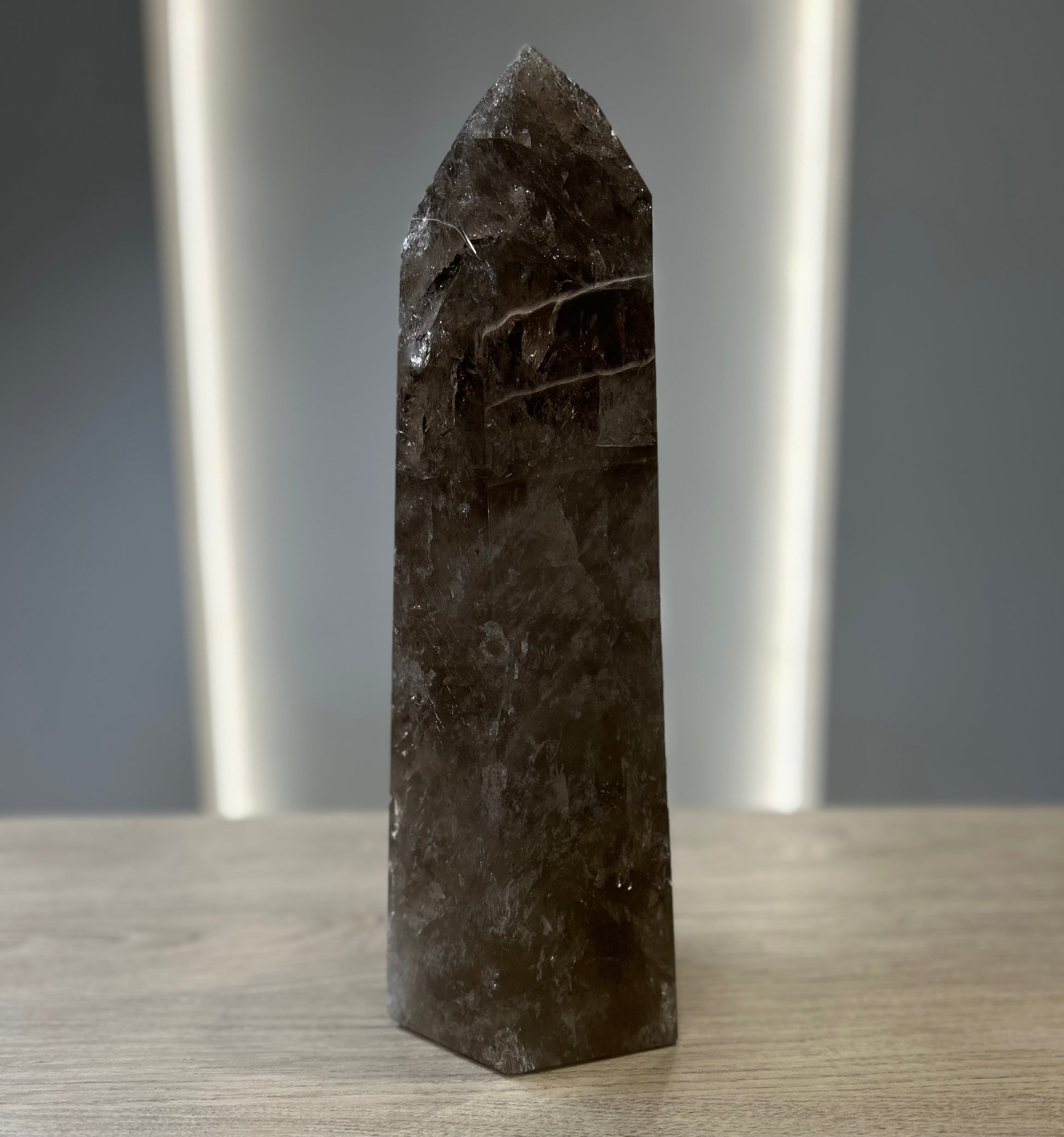 Smoky Quartz tower crystal on a wooden surface, known for its grounding and purifying properties.