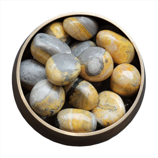 Bumble Bee Jasper tumbled stones in a bowl, showcasing vibrant yellow and gray patterns for energy and creativity boost.
