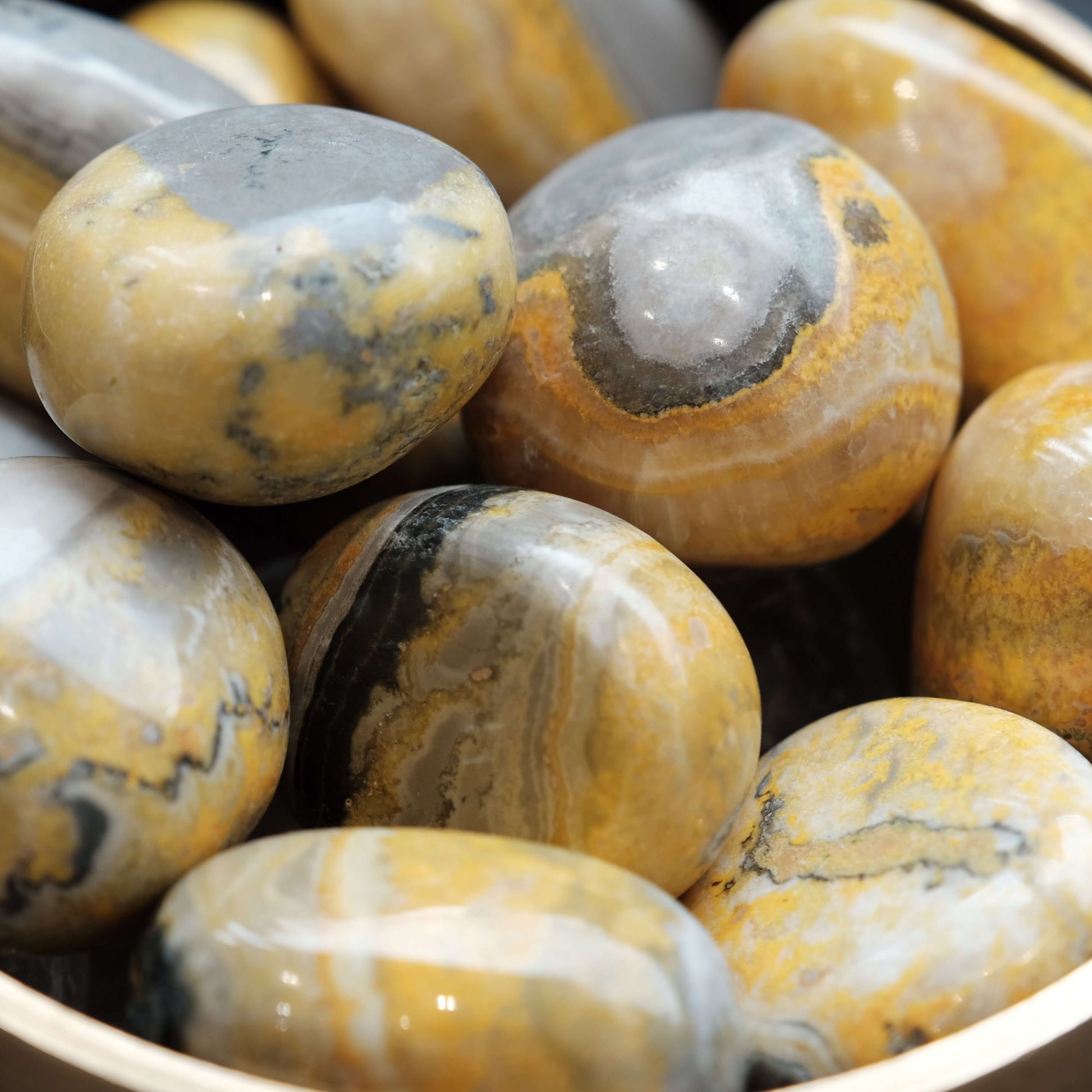 Bumble Bee Jasper tumbled stones in a bowl, showcasing vibrant yellow and gray patterns, ideal for energy and creativity boost.