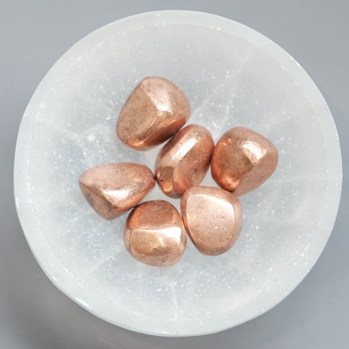 Copper tumbled stones on a round crystal dish, believed to boost energy and promote optimism and independence.