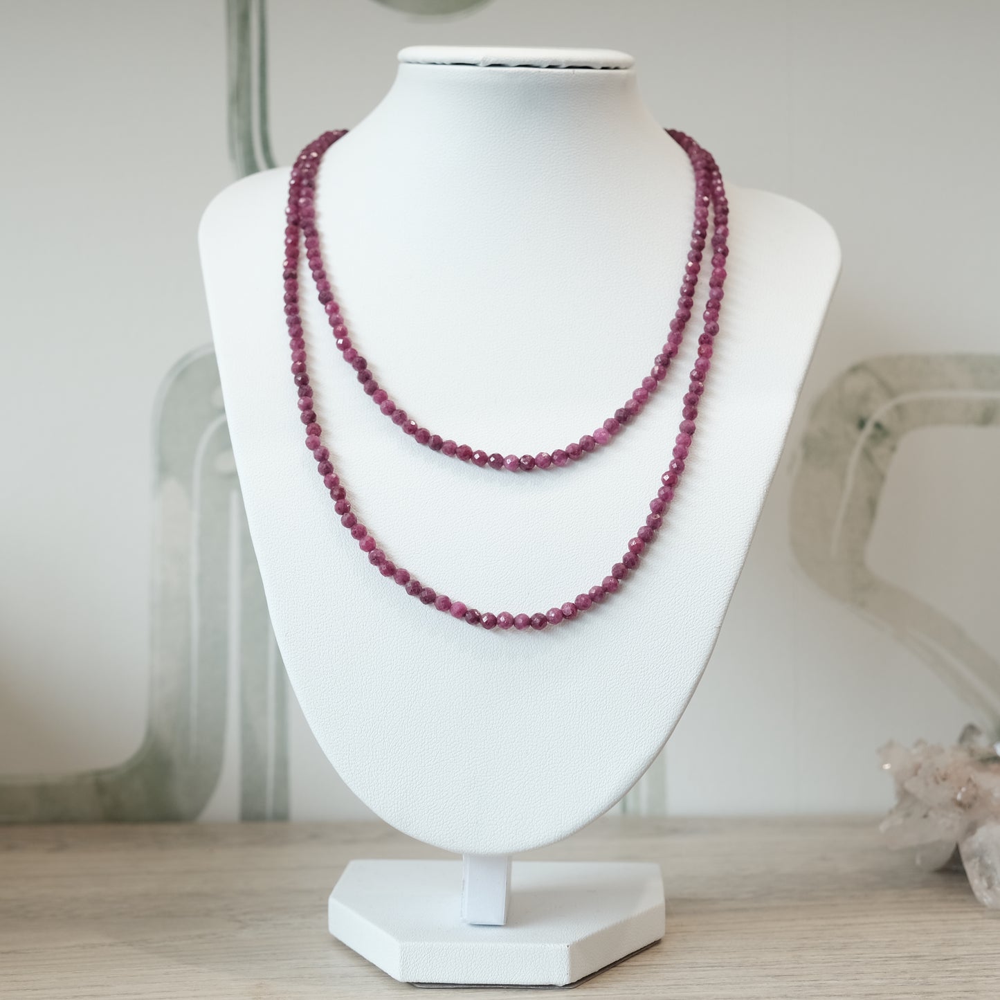 Elegant 31" ruby faceted necklace displayed on a white stand, versatile as a multi-wrap bracelet, showcasing deep red gemstones.