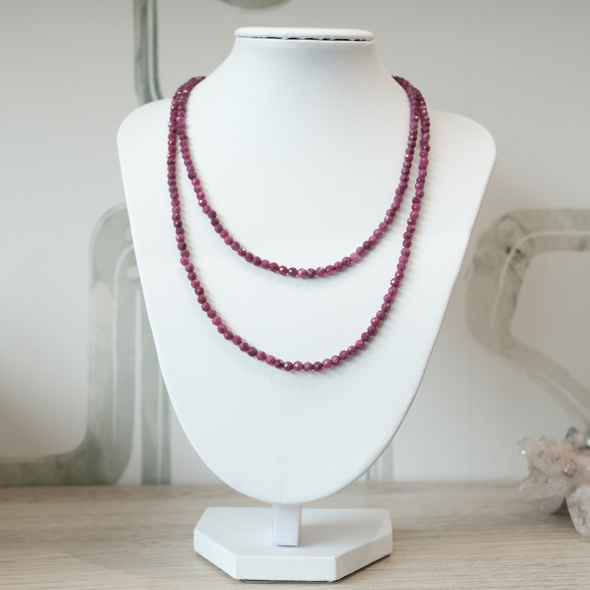 Elegant 31" ruby faceted necklace displayed on a white stand, versatile as a multi-wrap bracelet, showcasing deep red gemstones.