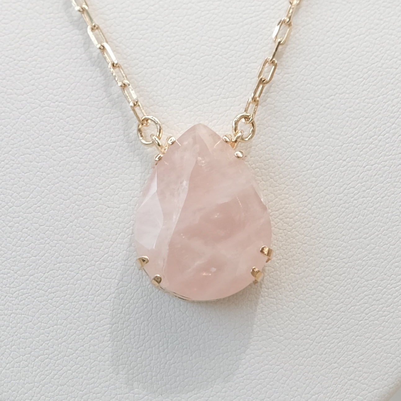 Rose quartz drop necklace with gold chain, featuring a teardrop-shaped pendant on a textured background.