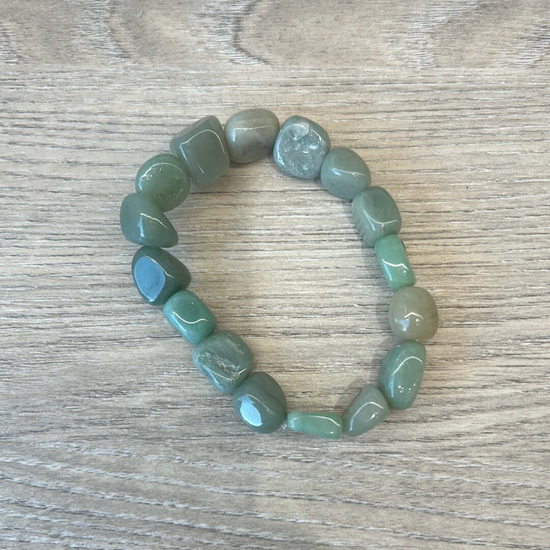 Green Aventurine pebble bracelet on wooden surface, promotes balance and clears negative energy with healing properties.