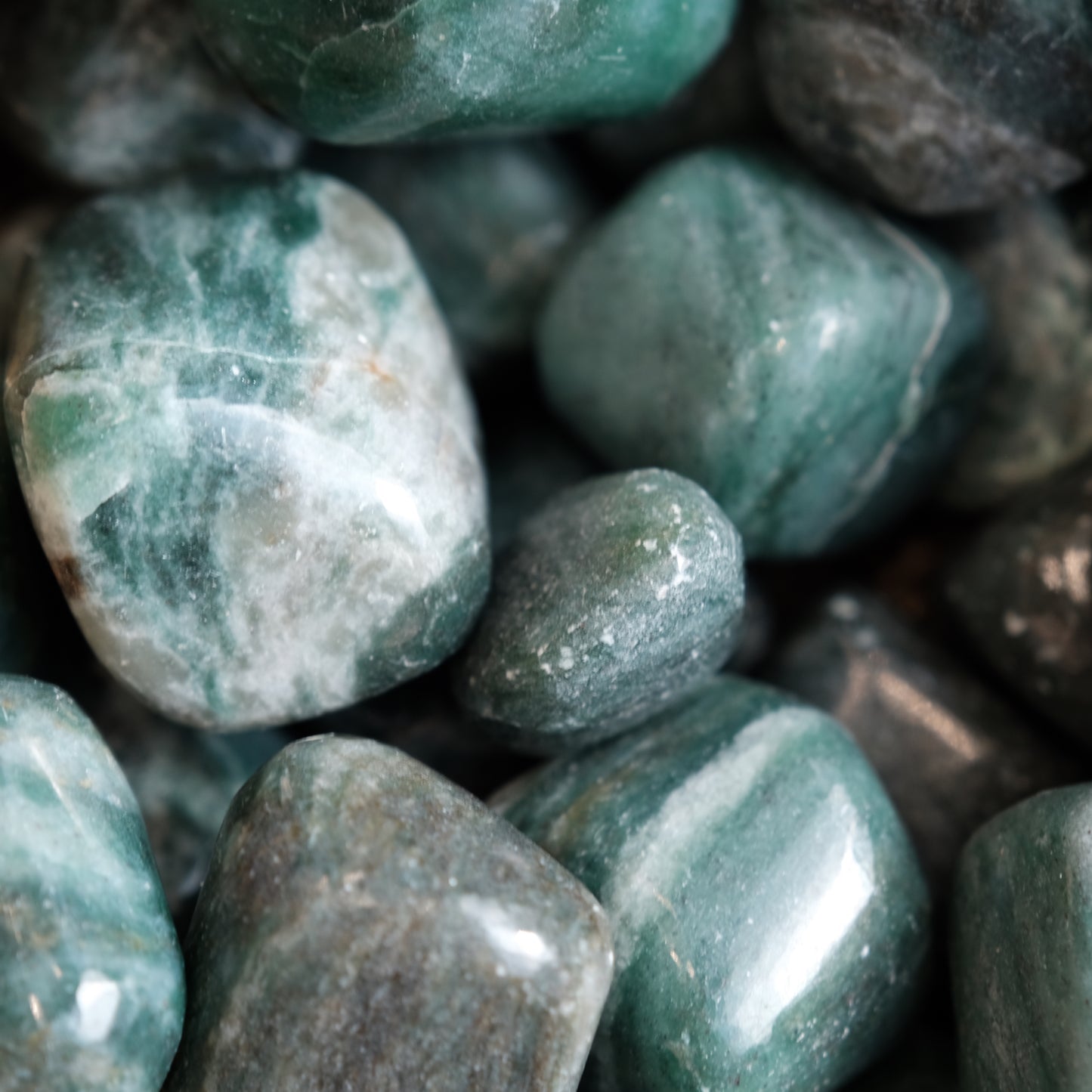 Close-up of emerald with fuchsite tumble stones, showcasing their green hues and smooth, polished surfaces for emotional healing.