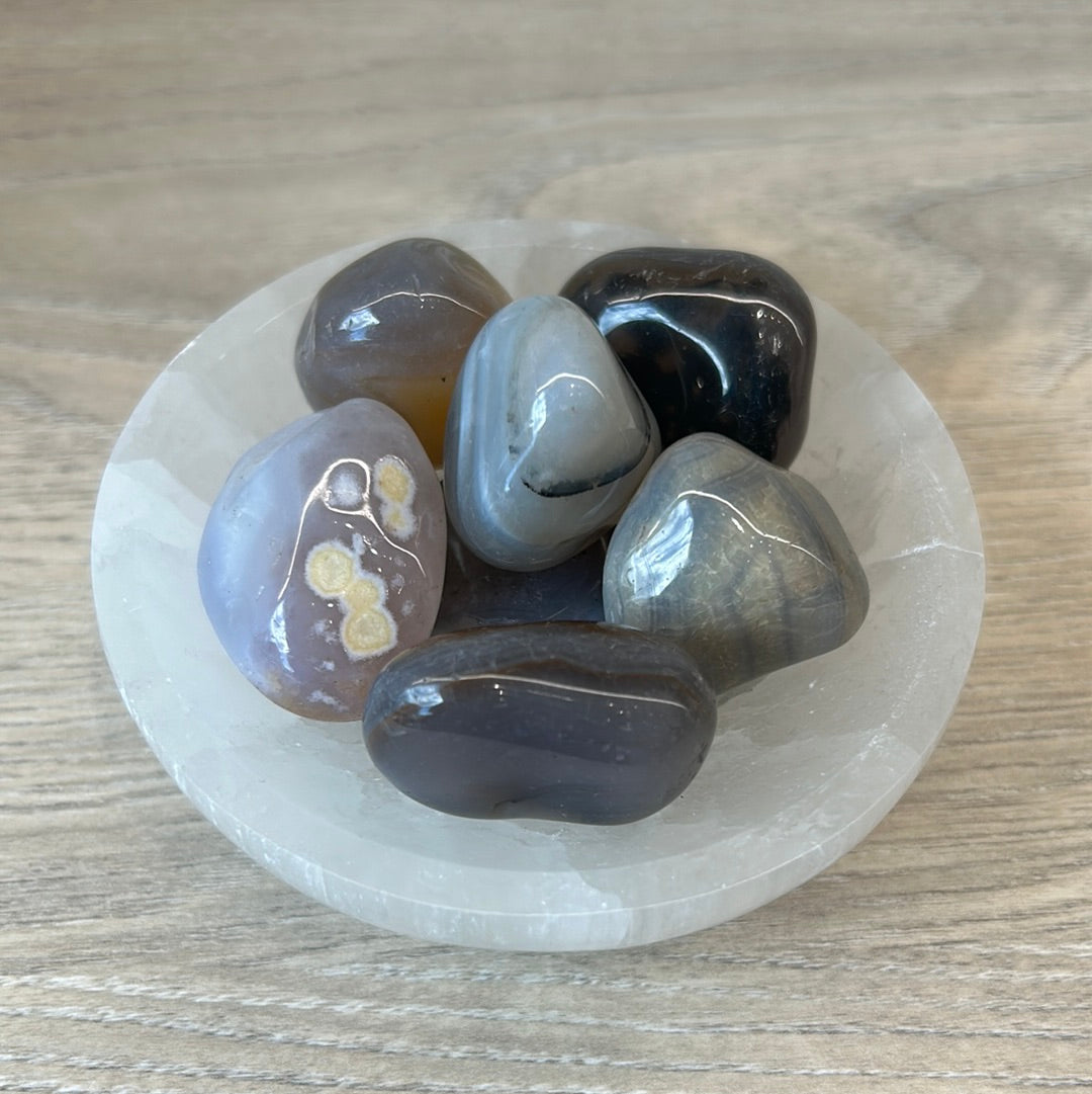 A collection of polished agate tumbled stones in a white dish on a wooden surface.