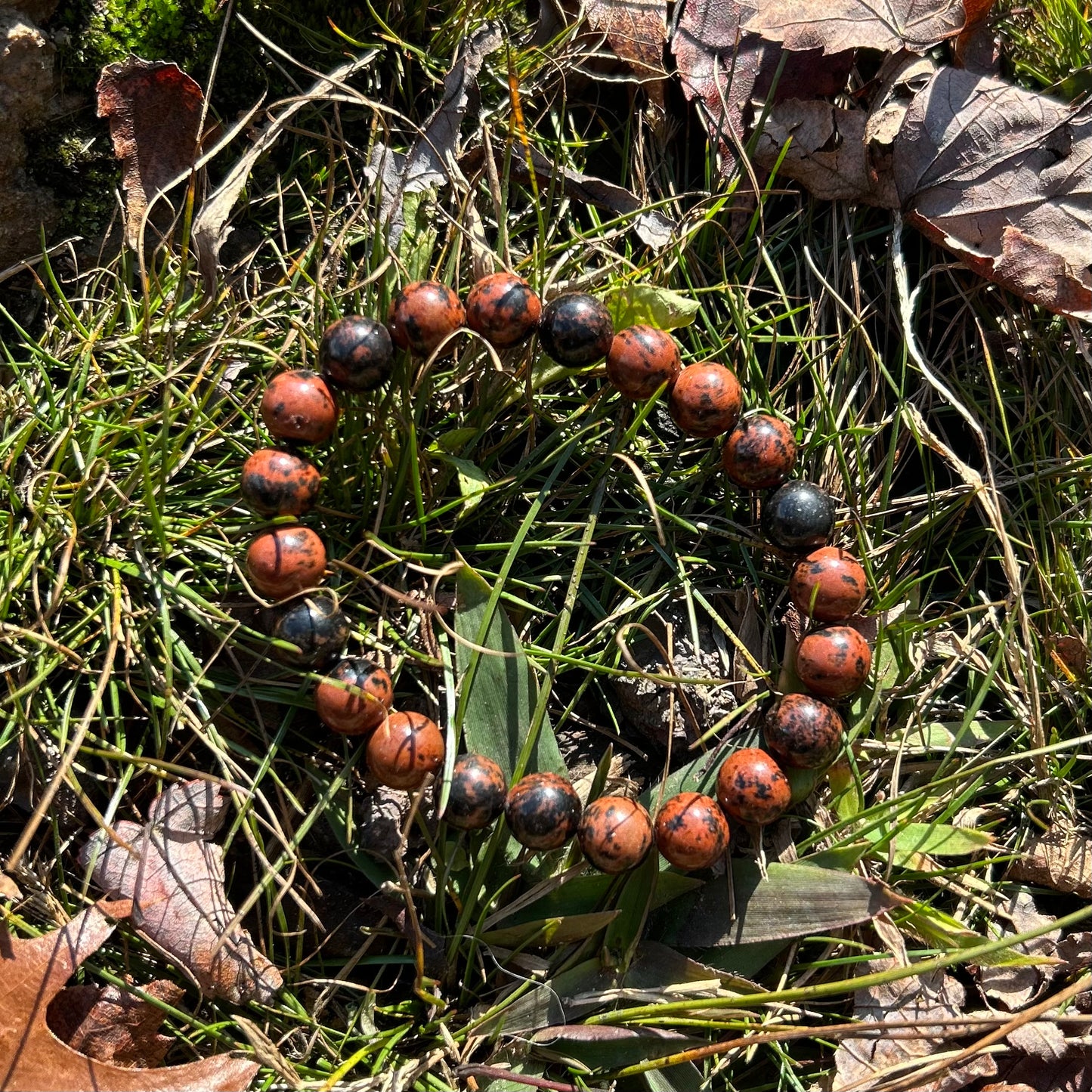 Mahogany obsidian bracelet 8MM displayed on grass and leaves, showcasing its polished finish and natural beauty.