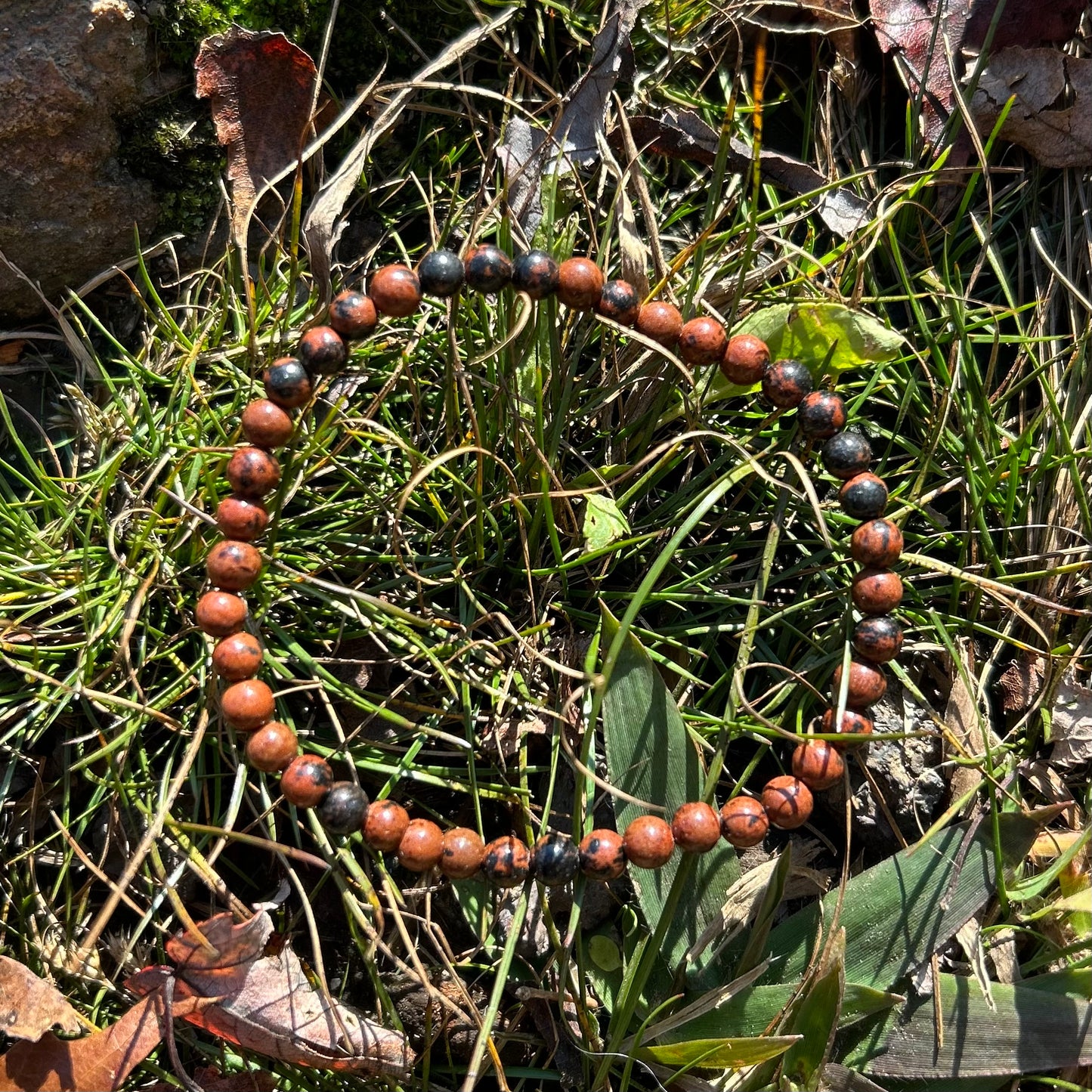 Mahogany Obsidian Bracelet 4MM on grass, showcasing its polished finish and natural healing properties.