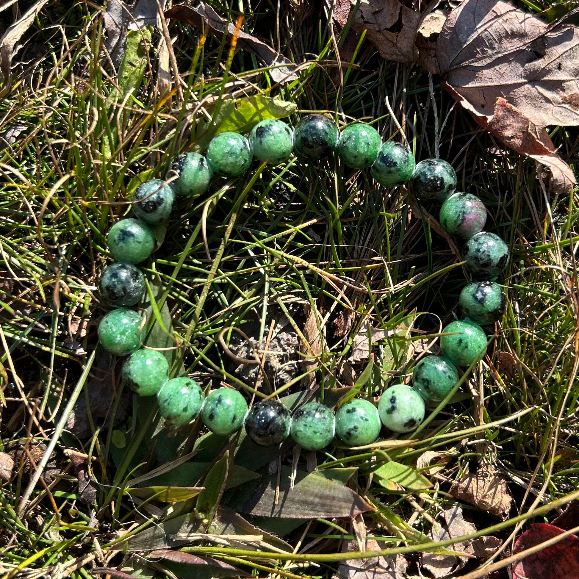 Ruby zoisite bracelet, 8mm beads, displayed on grass with autumn leaves, featuring vibrant green and red hues.