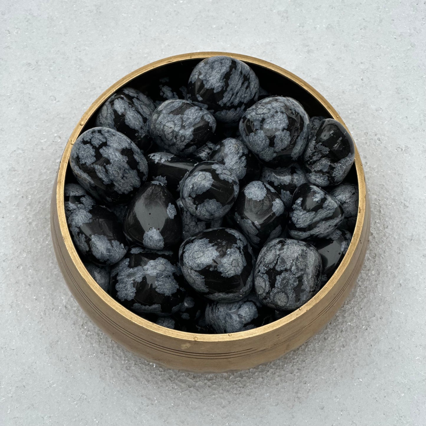 Snowflake Obsidian tumbled stones in a bamboo bowl, promoting calmness and self-reflection for meditation.