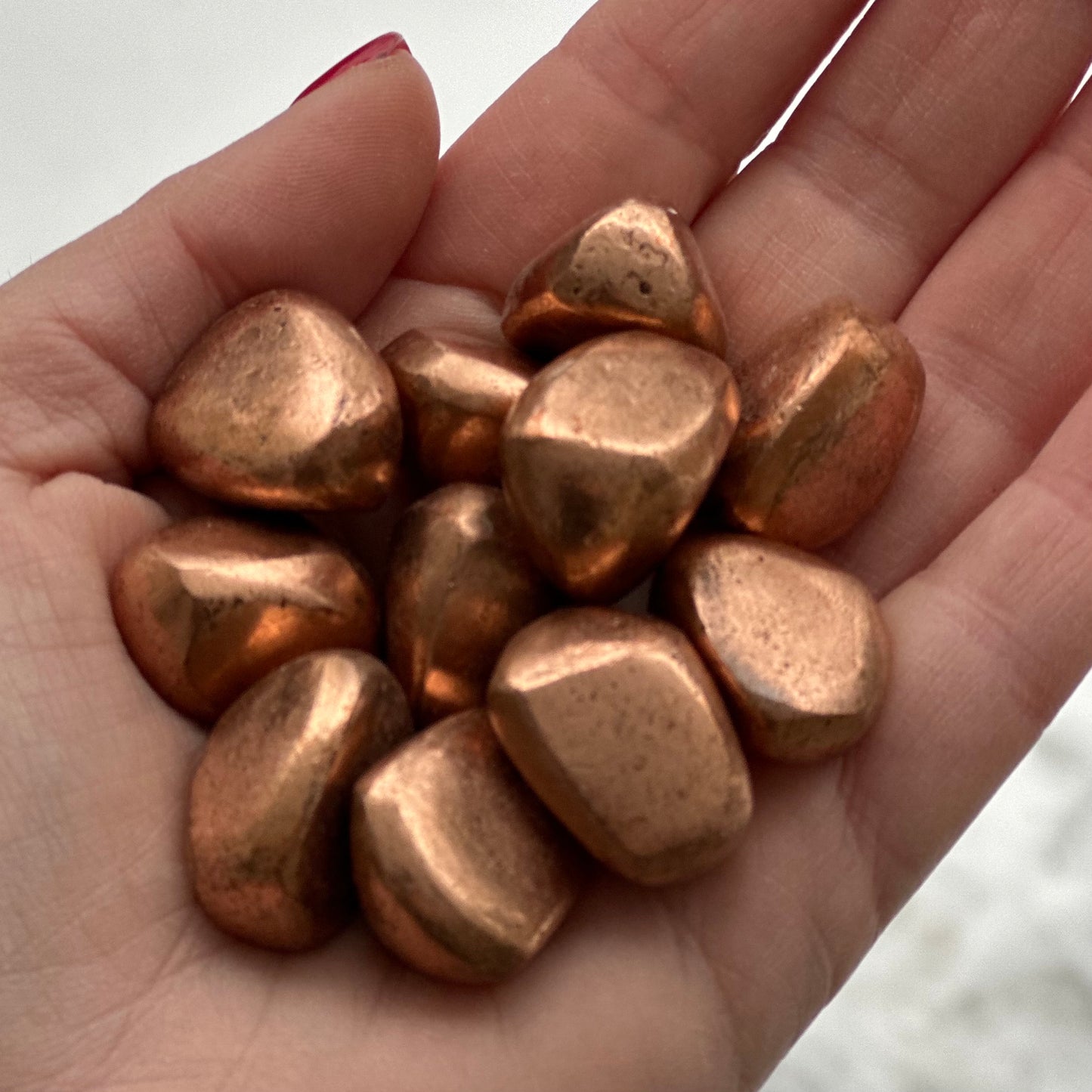 Hand holding copper tumbled stones, believed to enhance energy and promote optimism and independence.