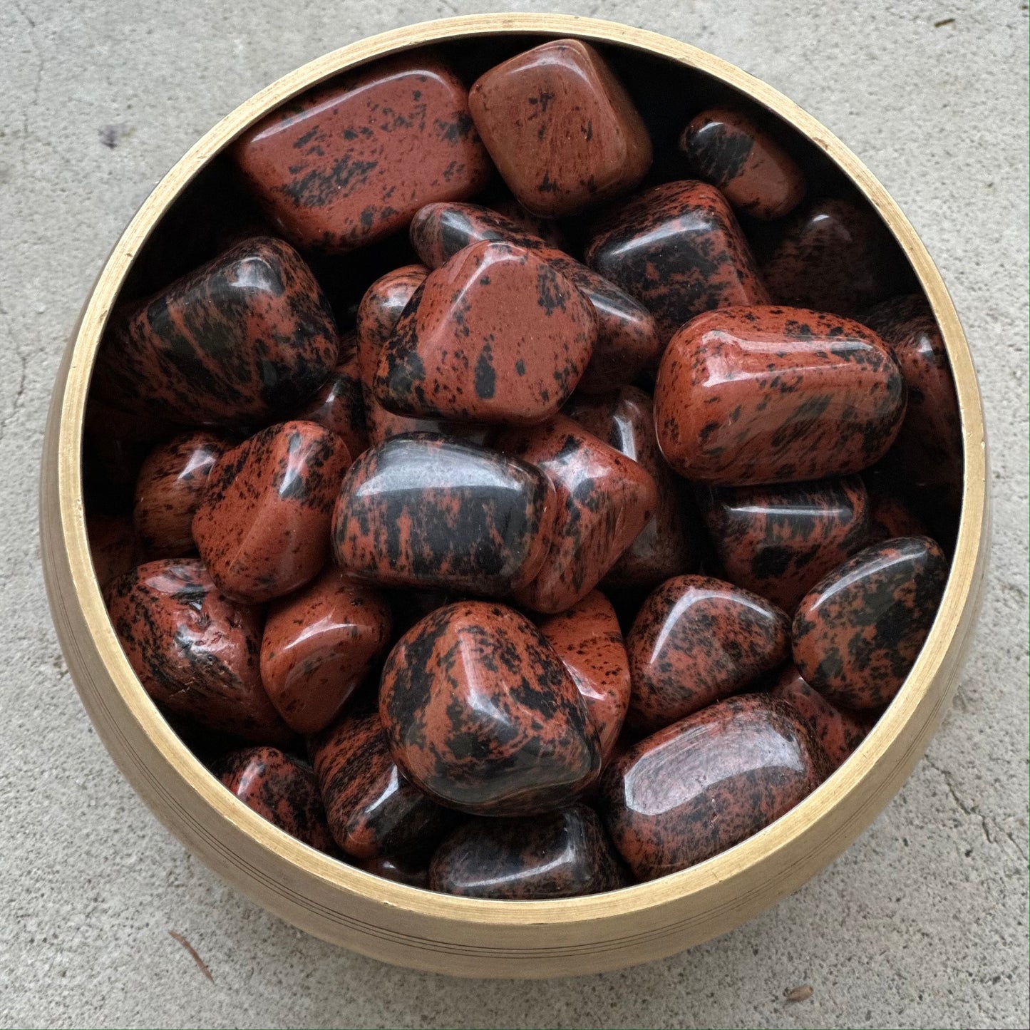 Mahogany Obsidian tumbled stones in a bamboo bowl, showcasing their rich, earthy tones and smooth textures.