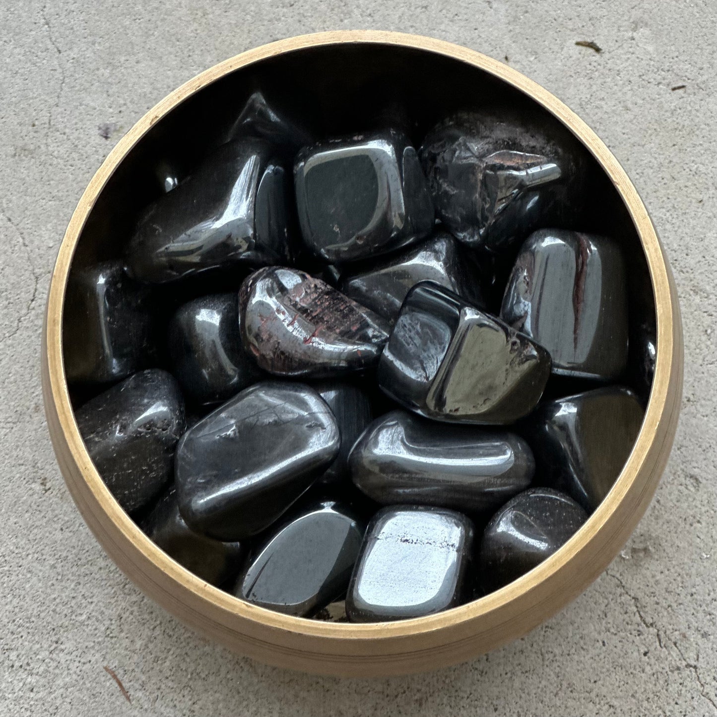 Hematite tumbled stones in a wooden bowl, showcasing grounding and protective energy properties for focus and clarity.
