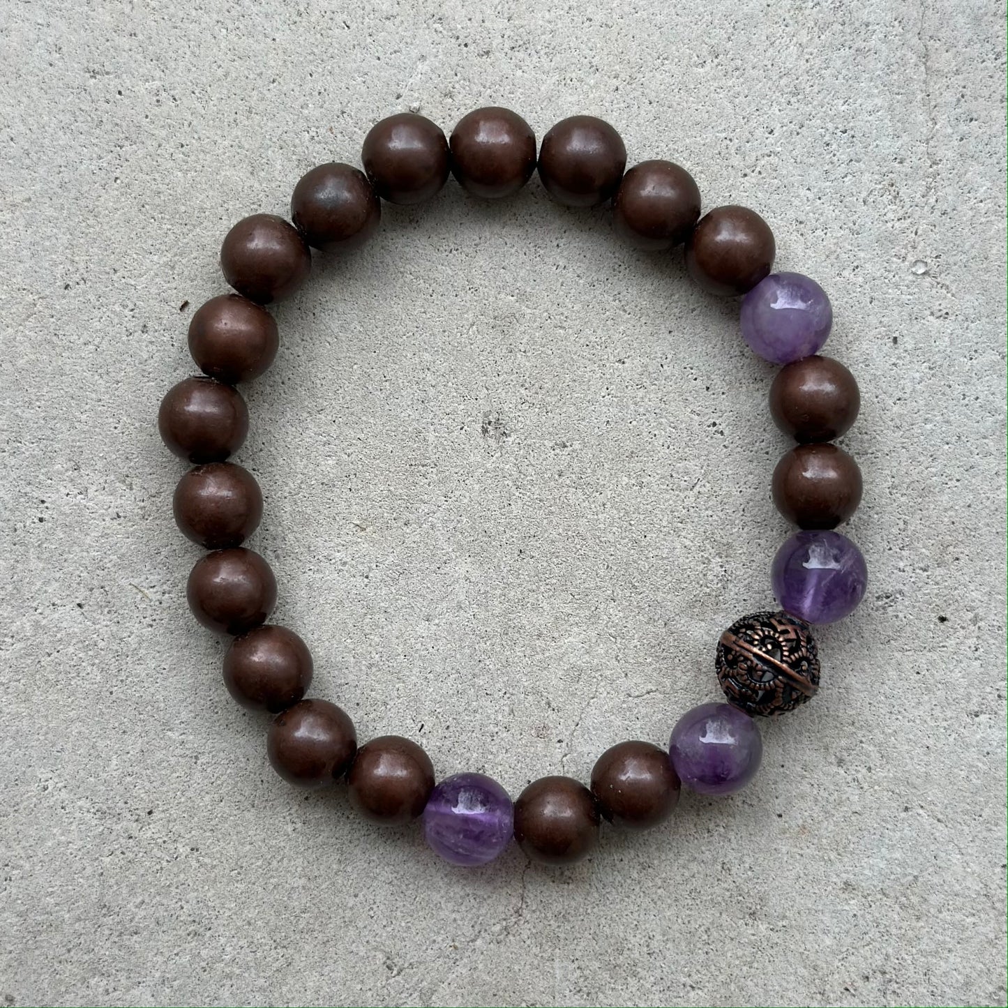 Copper and amethyst bead bracelet on a neutral background, designed for energy healing and promoting optimism and independence.