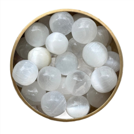 Round selenite tumbled stones in a wooden bowl for meditation and spiritual clarity.