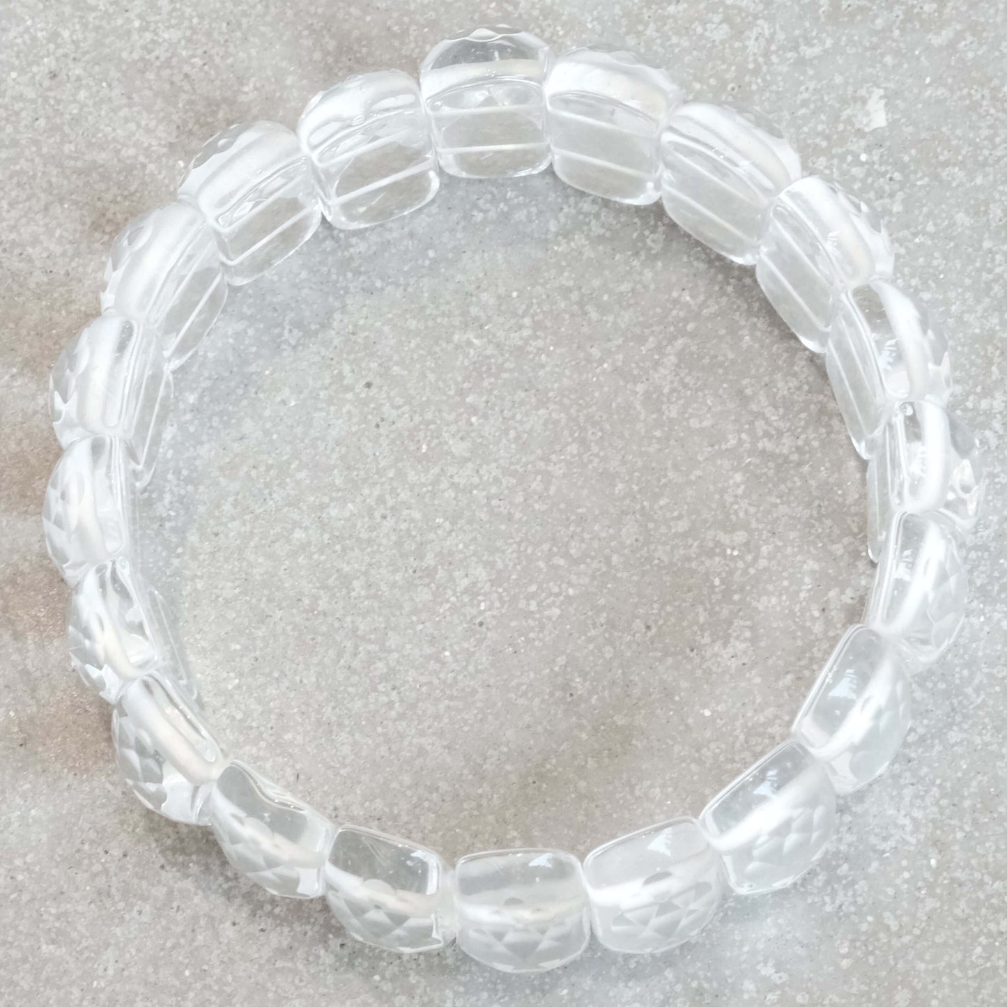 Clear Quartz Faceted Bracelet 24MM featuring transparent beads, elegantly arranged on a textured stone background.